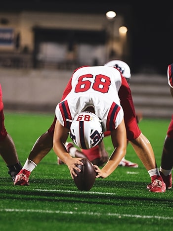 Brayson Albin, number 68, in his long snapper stance over the ball under the lights
